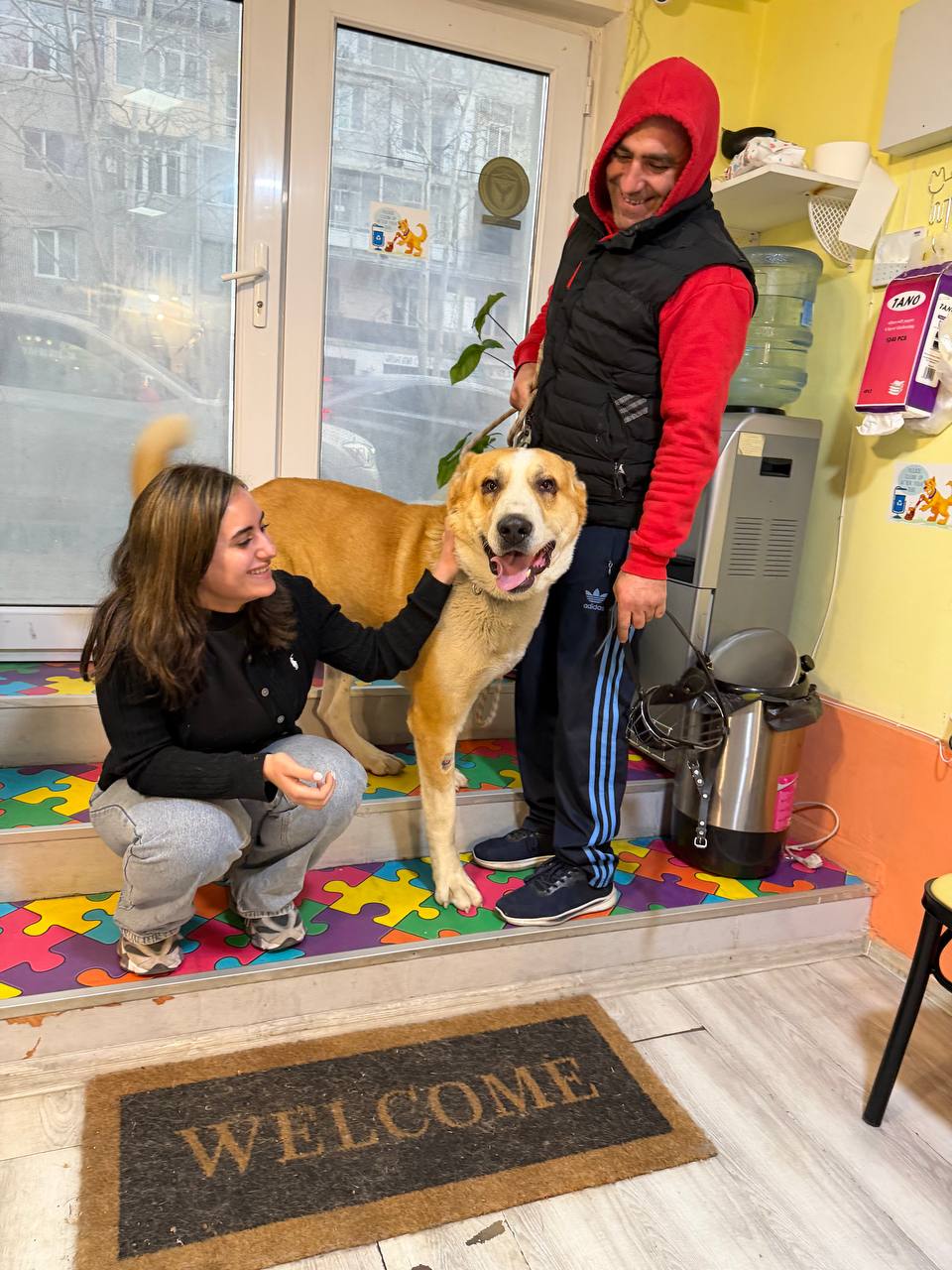 Owner and staff member petting a large mixed-breed dog by the entrance